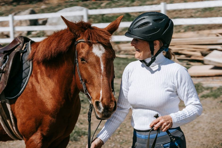 Une personne consulte son téléphone en tenue d’équitation, sac sur l’épaule, avant de partir