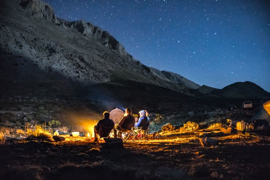 Des amis à l’apéro autour d’un feu de camp, bivouac en montagne sous les étoiles — là où l’idée est née